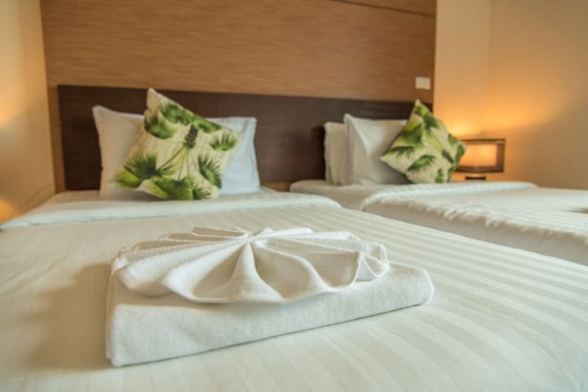 Habitación de hotel con dos camas, cada una con una colcha blanca y una toalla blanca doblada cuidadosamente. Dos almohadas con un estampado de hojas tropicales en los cabeceros.
