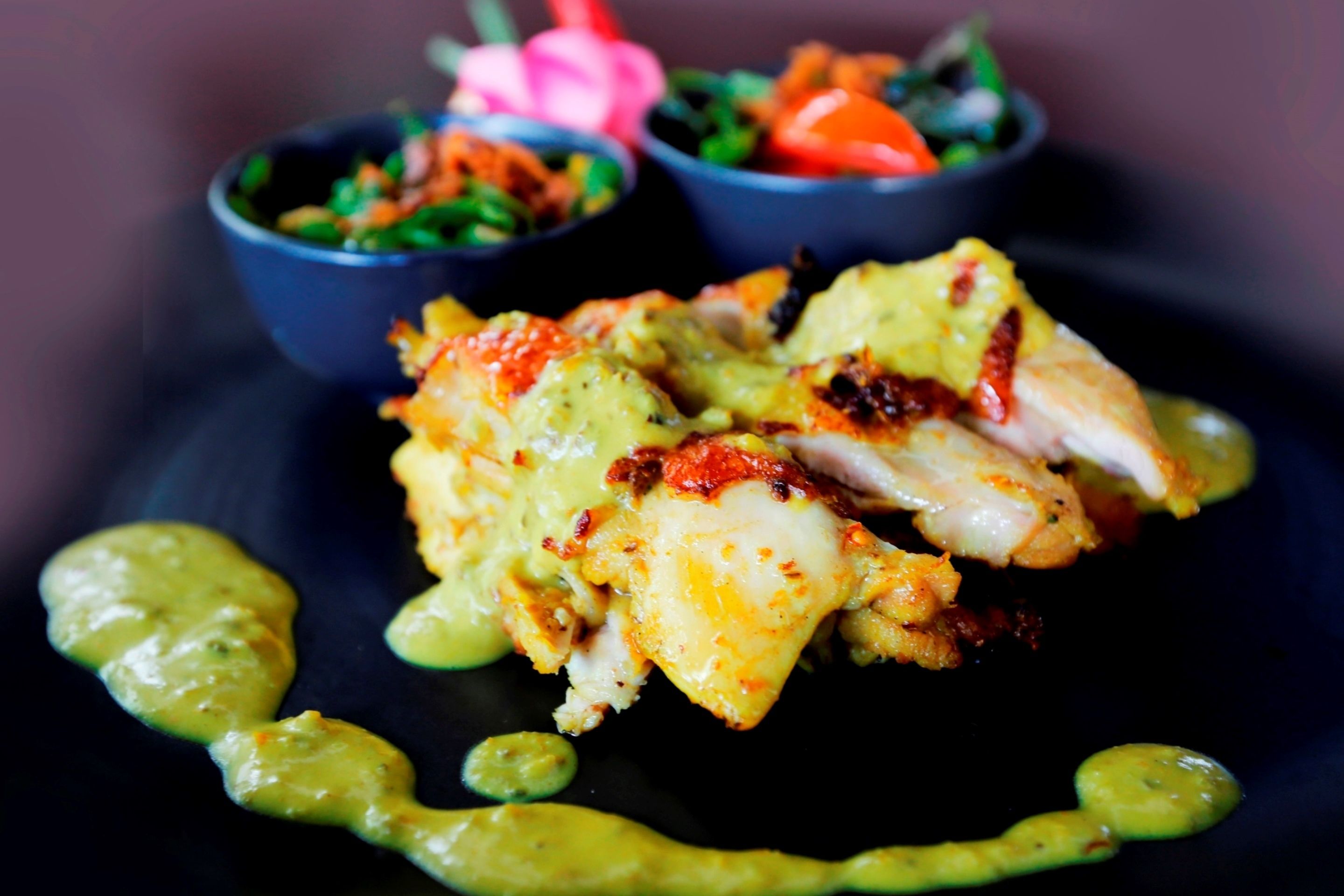 Un plato de comida con salsa verde, ensalada y una flor rosa.