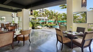 A spacious indoor area with a dining table and chairs, a ceiling fan, and a view of a pool and greenery outside. - Bali Nusa Dua Hotel (Nusa Dua)