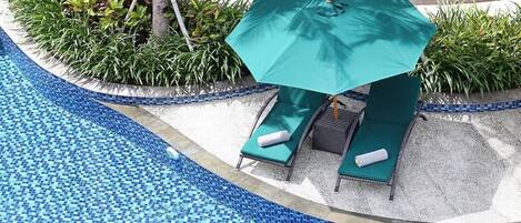 A poolside area with a green umbrella, two lounge chairs, and a small garden with various plants.