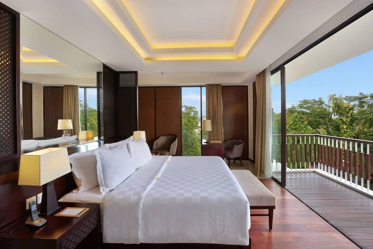 Une chambre d’hôtel avec un grand lit, des tables de chevet, un bureau, une chaise, un balcon avec une rambarde et une grande fenêtre.