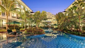 A hotel pool area with a tiled pool, lounge chairs, and palm trees. - Bali Nusa Dua Hotel (Nusa Dua)