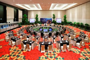 A large conference room with a circular table surrounded by chairs, a red carpet, and two large screens on the walls.