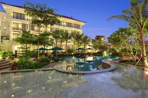 A hotel with a swimming pool, palm trees, and outdoor seating areas.