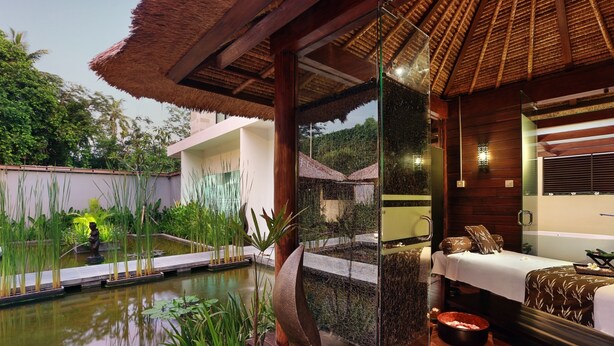 A spa room with a wooden floor, a thatched roof, a massage table, a small pool, and a decorative sculpture. - Bali Nusa Dua Hotel (Nusa Dua)