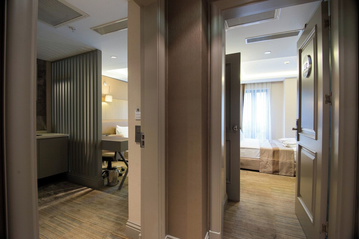 A hotel room with a bed, bedside table, and a bathroom with a sink and mirror.