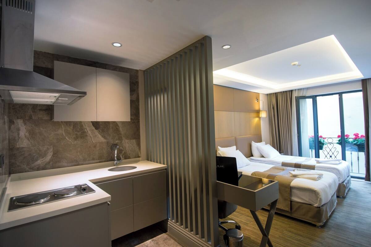 A modern hotel room with a kitchenette, a bed with a view, and a separate seating area.