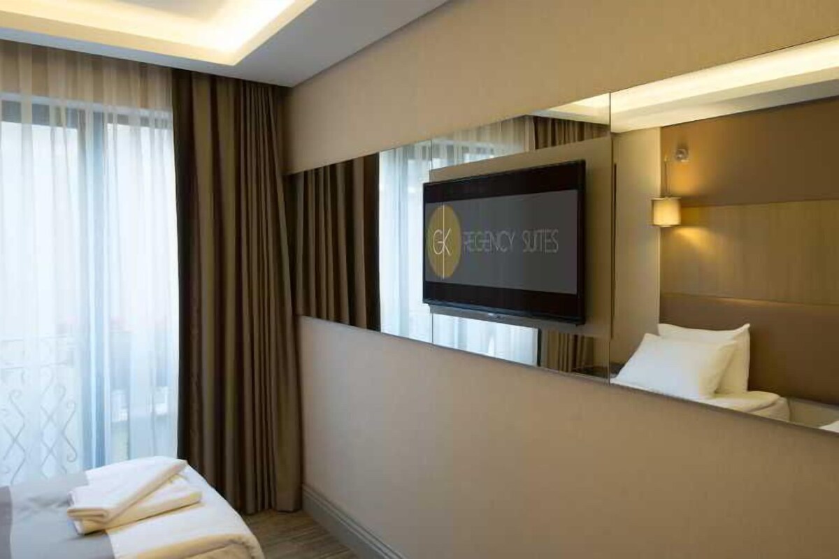 A hotel room with a bed, a TV, a large mirror, and a window with curtains.