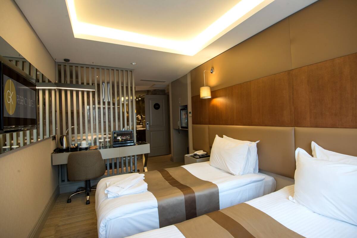 A hotel room with two beds, a desk, a chair, a TV, and a minibar.