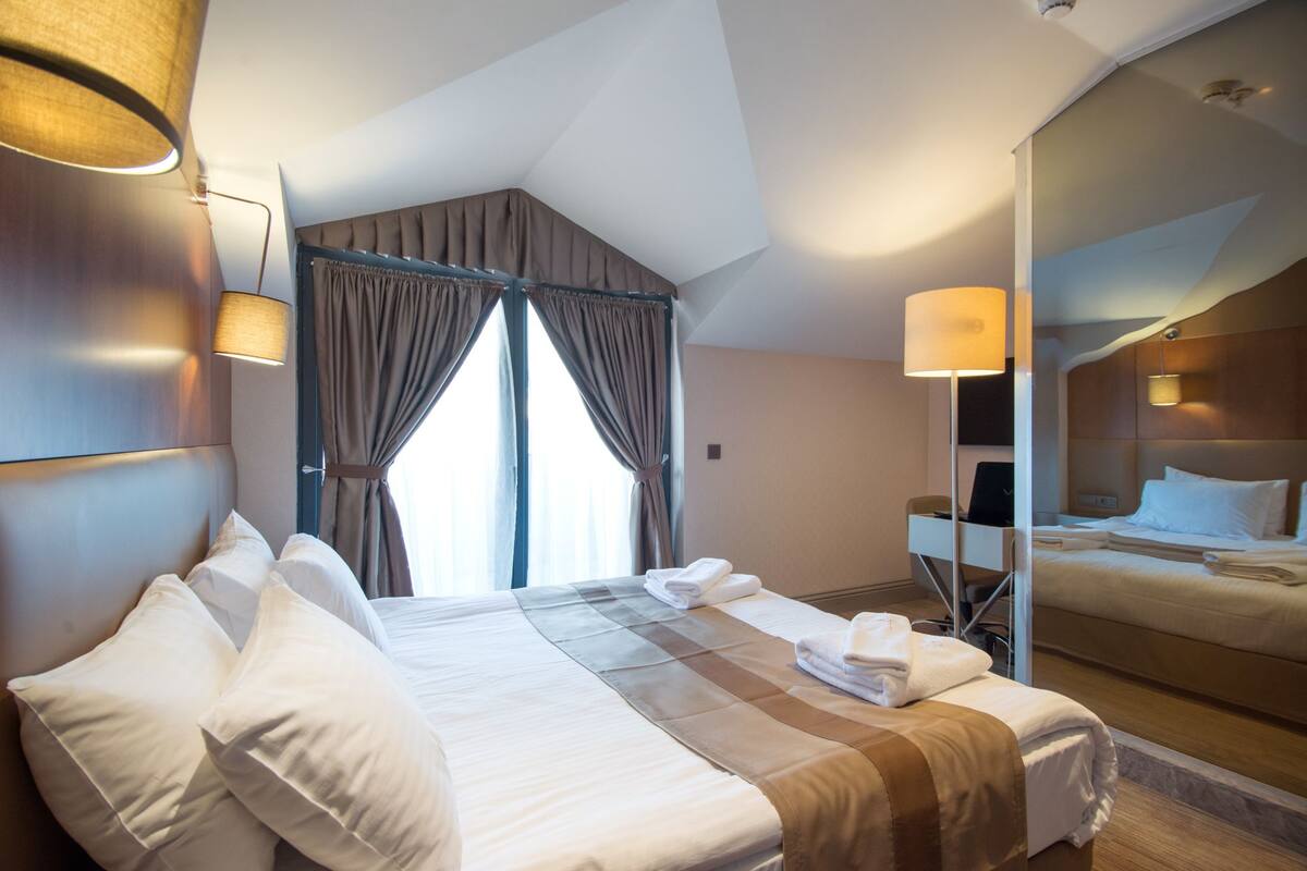 A hotel room with a large bed, a desk, and a mirror.