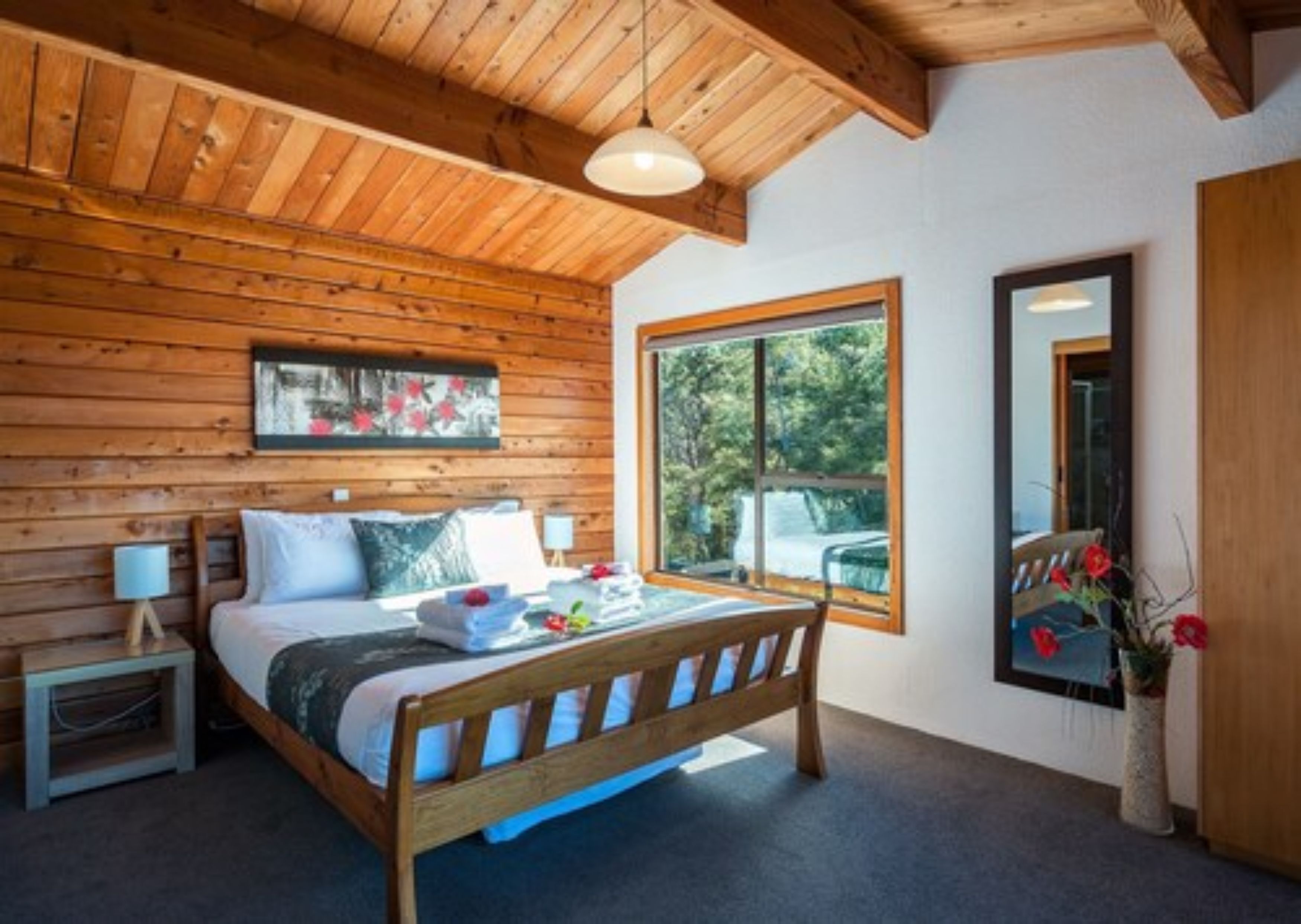 A wooden-paneled bedroom with a bed, a bedside table, a window, and a mirror.