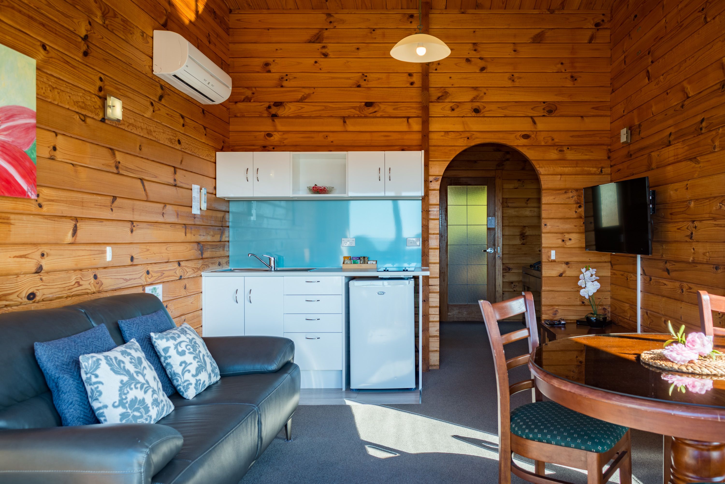 A cozy cabin interior with a wooden interior, a kitchenette, a dining area, and a living room with a sofa and chairs.