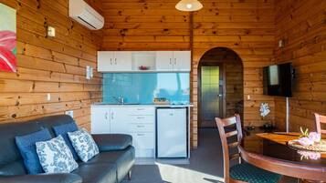 A cozy cabin interior with a wooden interior, a kitchenette, a dining area, and a living room with a sofa and chairs.