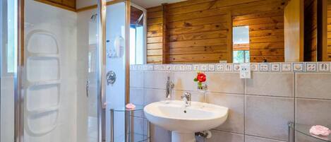 A bathroom with a glass-enclosed shower, a white sink, and wooden paneling on the walls.