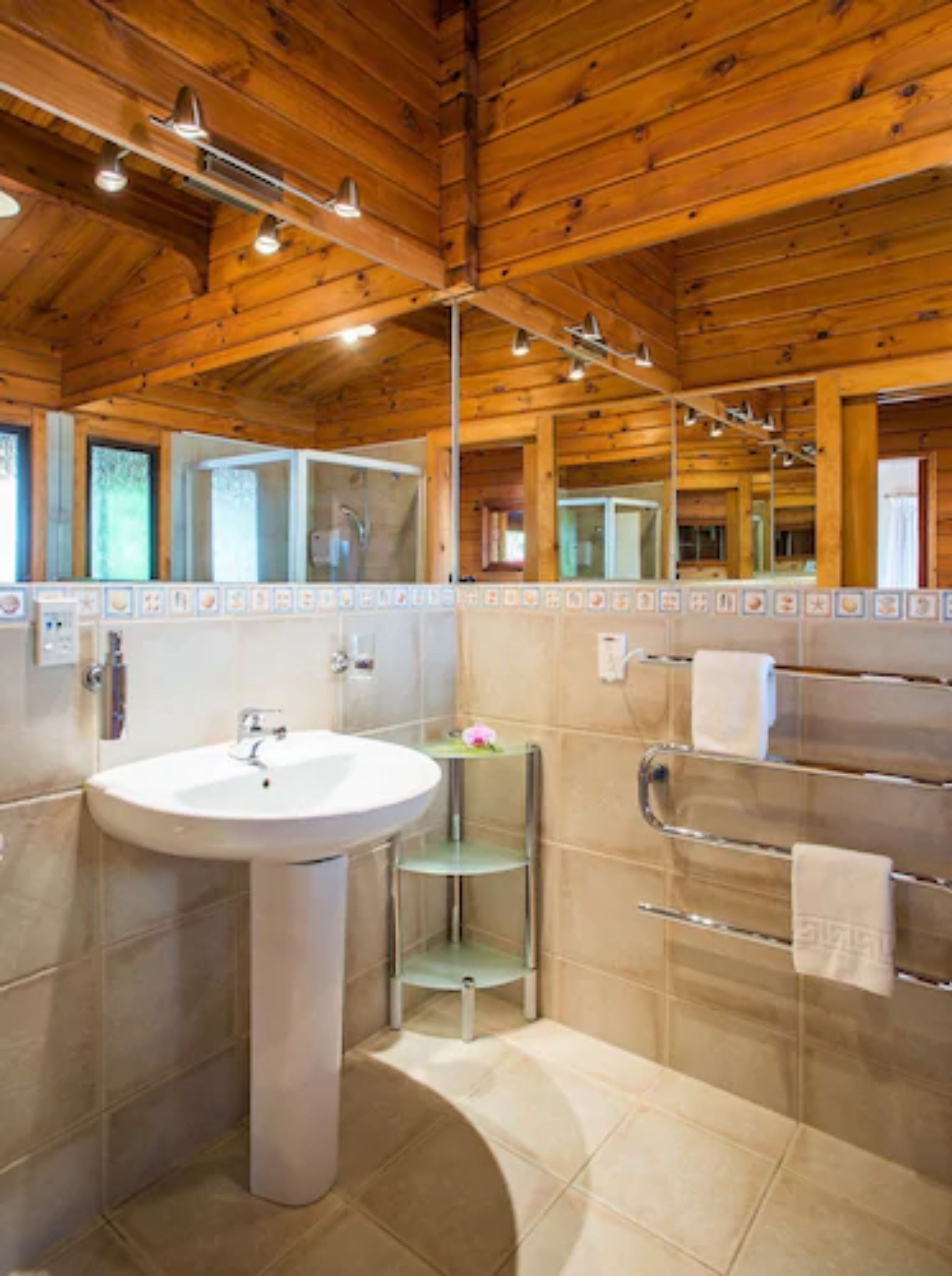 A bathroom with a wooden ceiling, a white sink, a glass shelf, and a towel rack.