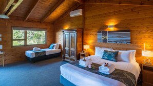 A log cabin bedroom with two beds, a wardrobe, and a large window. - Kimi Ora Eco Resort (Kaiteriteri)