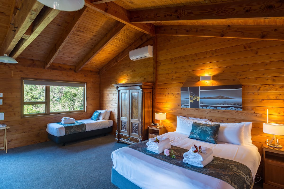 A log cabin bedroom with two beds, a wardrobe, and a large window.