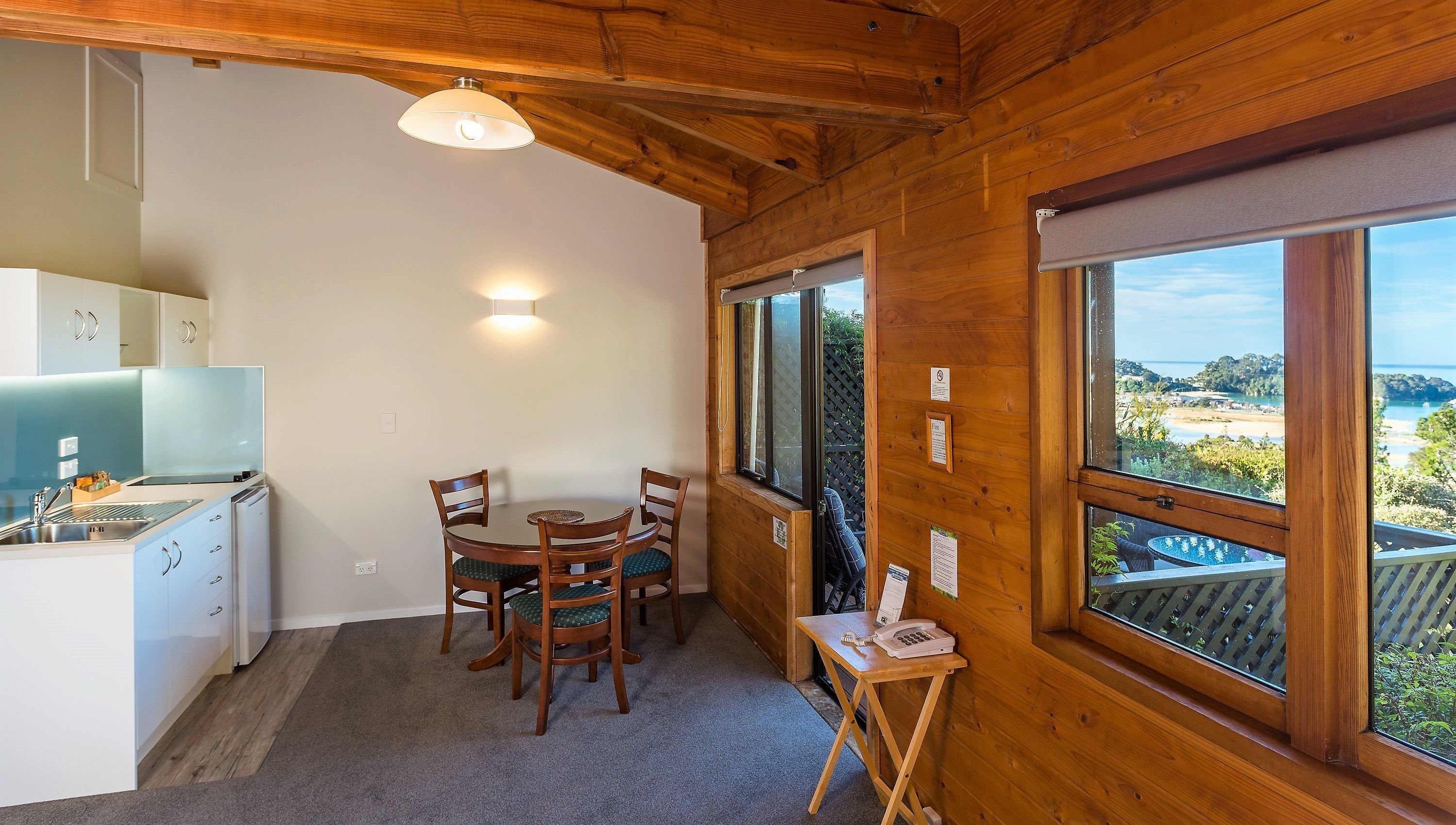A wooden interior with a kitchen, dining area, and large windows offering a view of the outdoors.