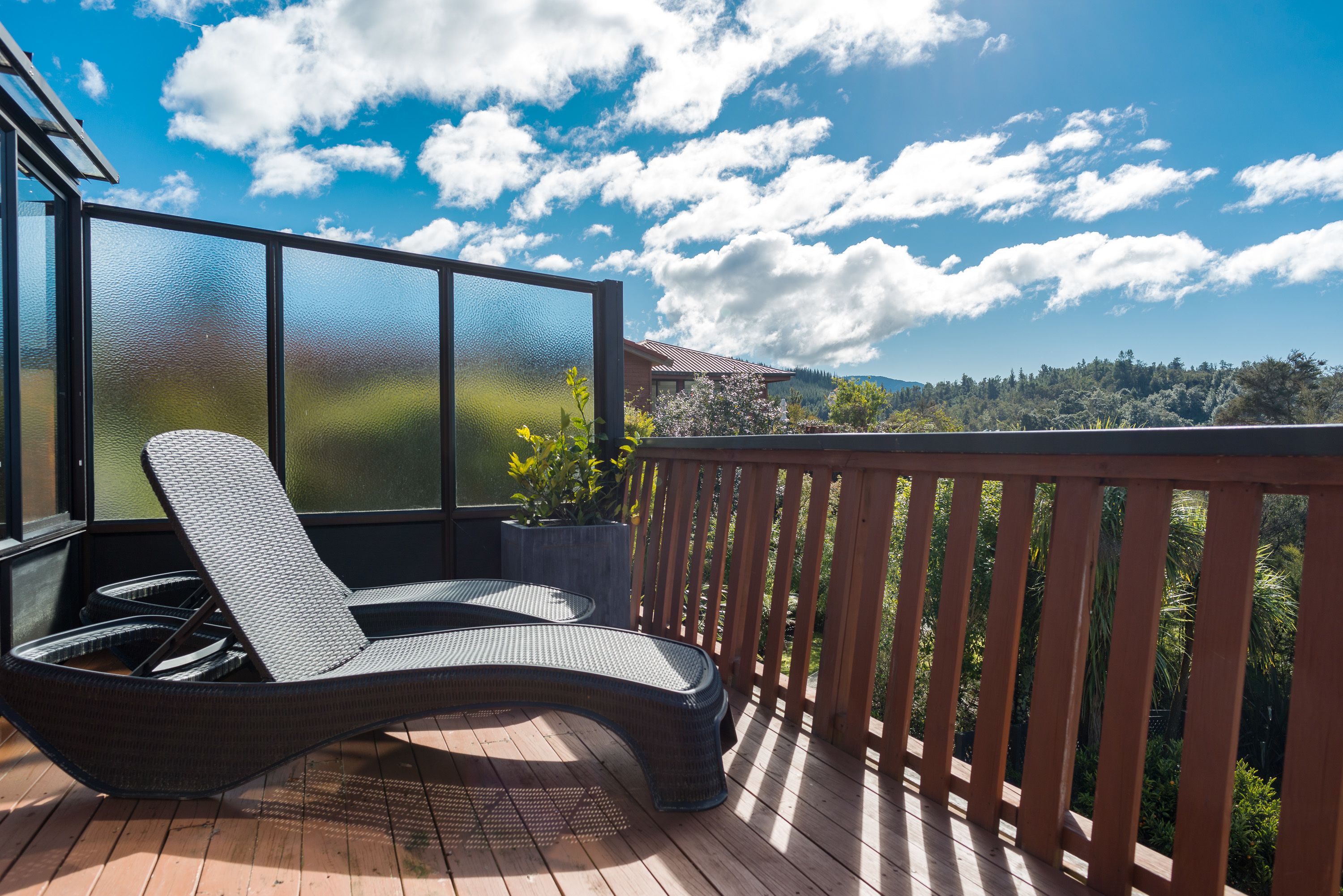 A balcony with a wicker lounge chair, a wooden railing, and a view of a mountainous landscape.