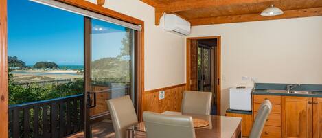 Una terraza de madera con una mesa y sillas, una cocina con armarios de madera, y vistas a un paisaje costero a través de amplios ventanales.