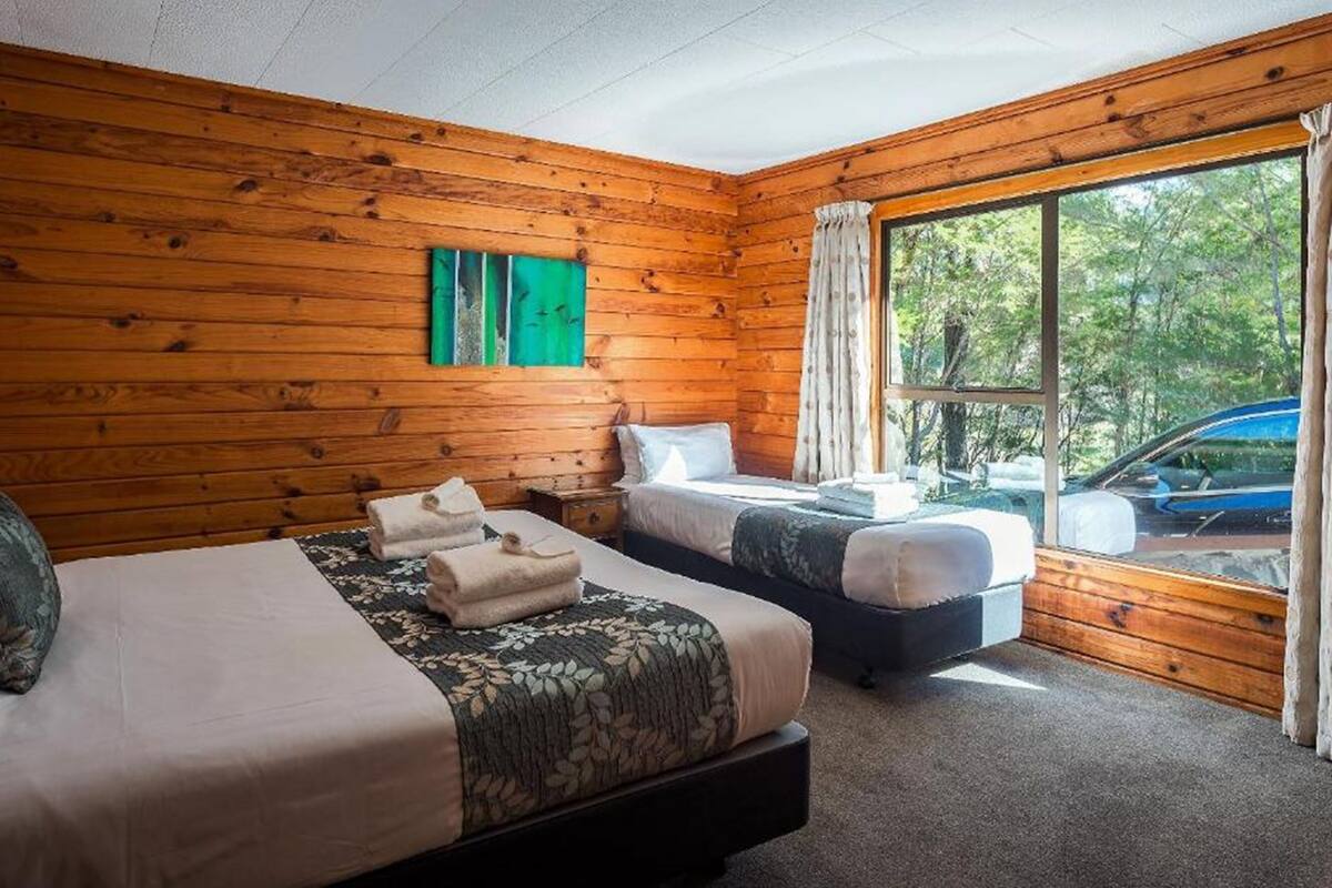 A room with two beds, wooden walls, a large window, and a view of the outdoors.