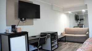 A modern hotel room with a flat-screen TV, a kitchenette, a sofa, and a mirror. - Relax Inn (Webster)