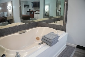 A modern bathroom with a large bathtub, a mirror, and a sink.