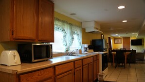 A kitchen with wooden cabinets, a microwave, a toaster, and a dining area with chairs and a table. - Relax Inn (Webster)