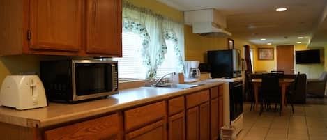A kitchen with wooden cabinets, a microwave, a toaster, and a dining area with chairs and a table.