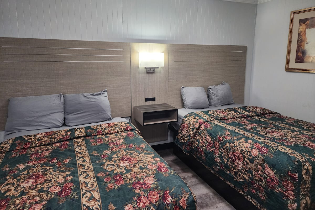 Camera d'albergo con due letti, ognuno con biancheria da letto floreale, un comodino, una lampada a parete e un quadro appeso alla parete.