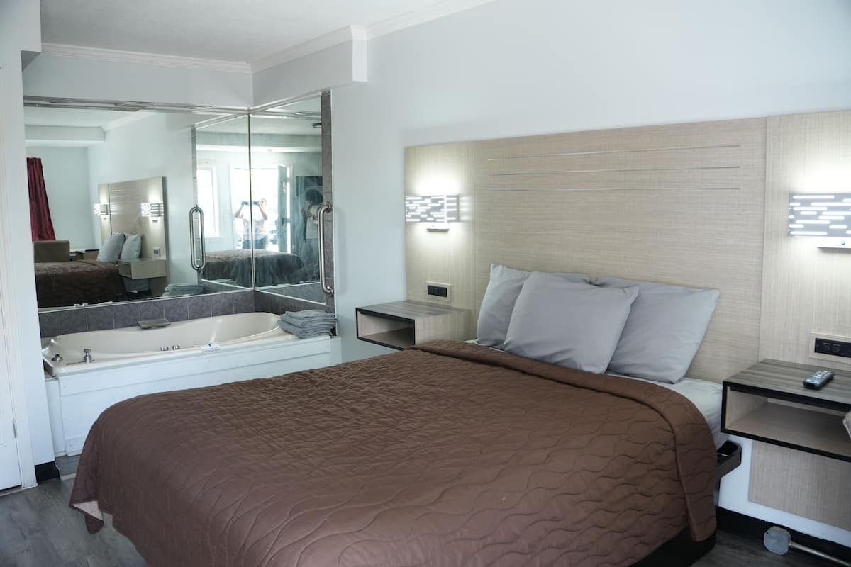 Una camera d'albergo moderna con un letto grande, un bagno separato con una vasca e uno specchio che riflette la stanza.