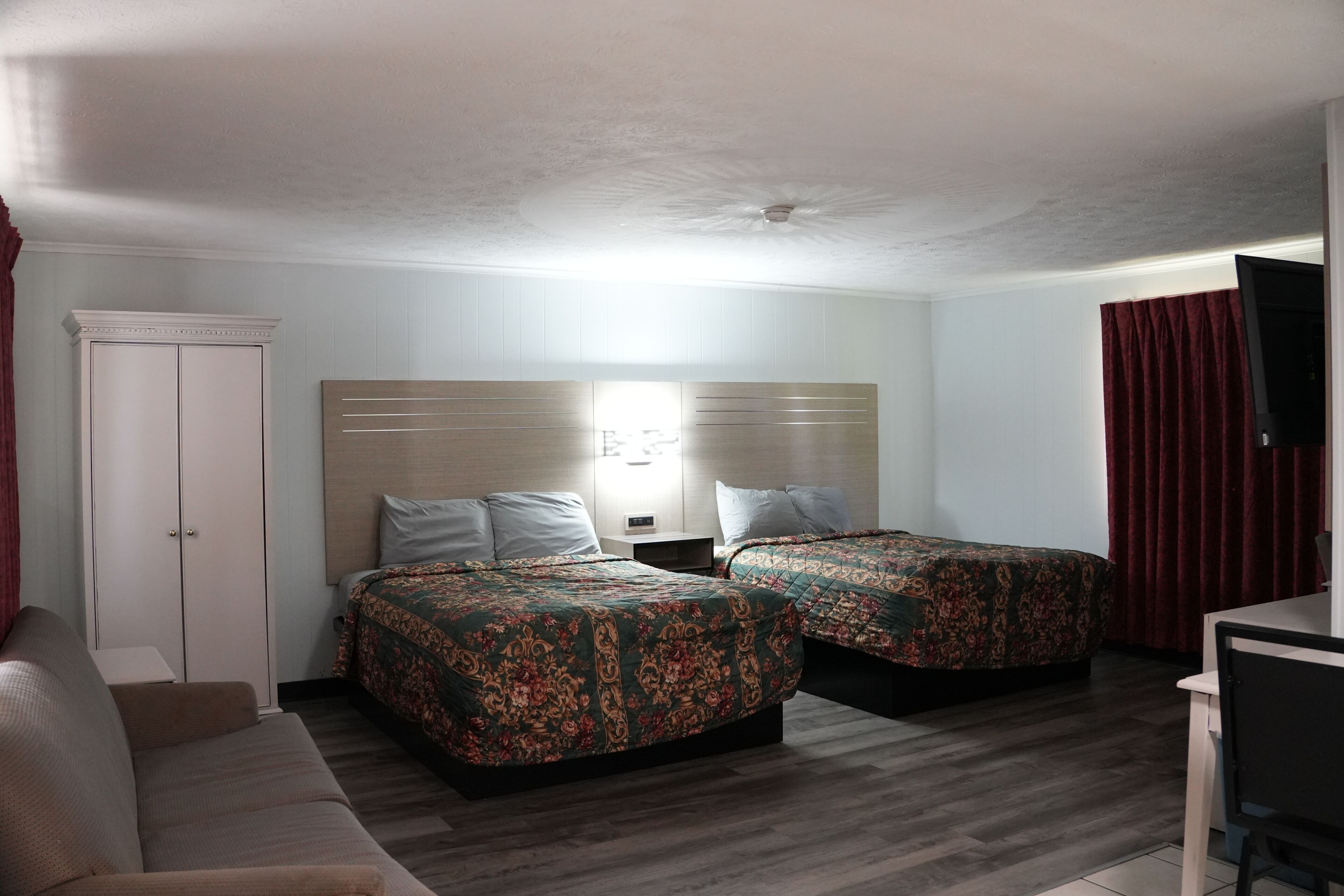 A hotel room with two beds, a sofa, a desk, and a wardrobe.