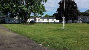 A grassy area with a white building, a tall white pole, and a tree. - Relax Inn (Webster)