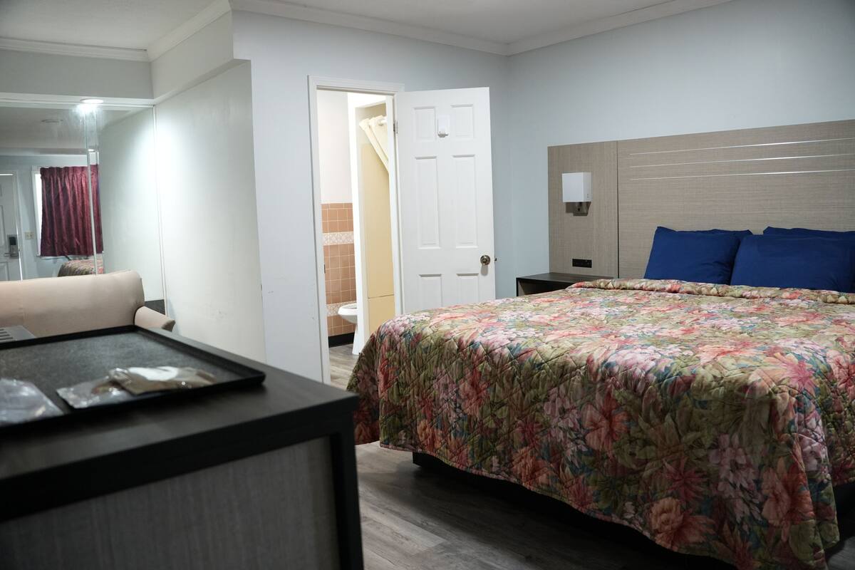 Una camera d'albergo con un letto, un comodino, uno specchio e una porta che dà sul bagno.