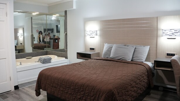 A modern hotel room with a large bed, a separate bathroom with a bathtub, and a large mirror. - Relax Inn (Webster)