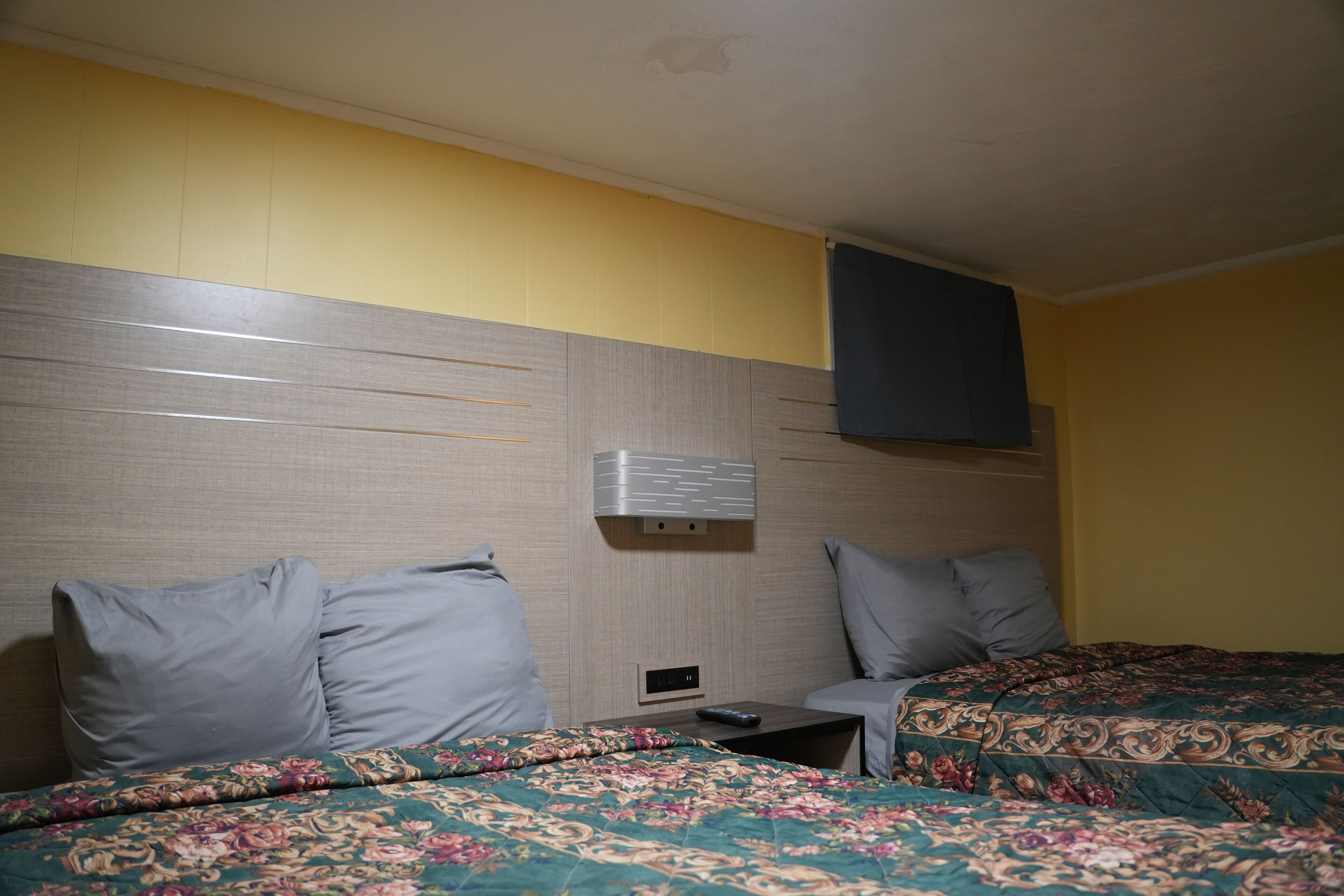 A hotel room with two beds, a nightstand, a wall-mounted air conditioning unit, and a small table.