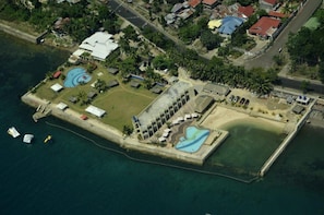An aerial view of a coastal resort with multiple swimming pools, a large building with a curved roof, and a dock with boats. - Danao Coco Palms Resort (Danao City)