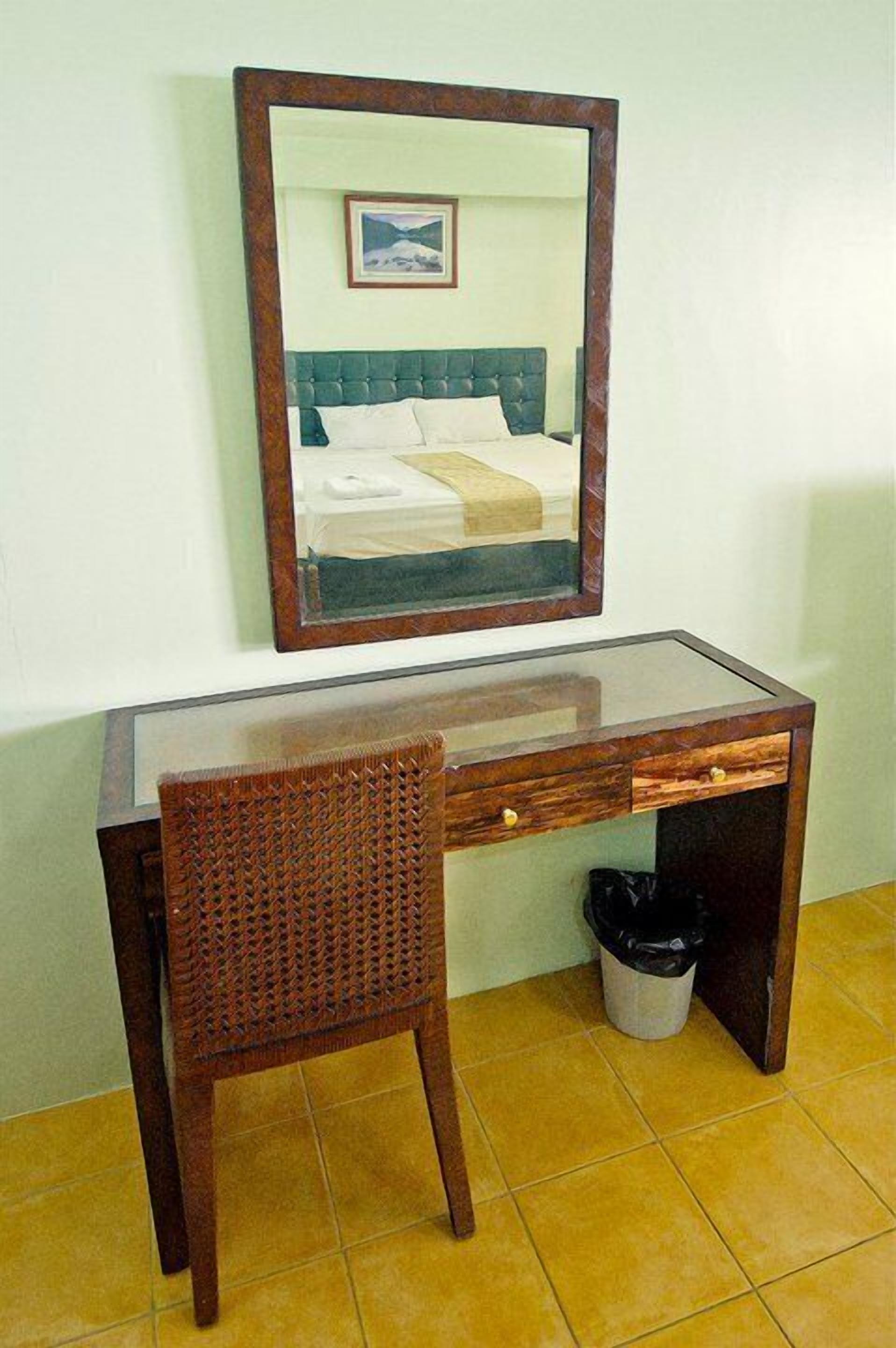 A wooden desk with a glass top, a wicker chair, and a mirror.