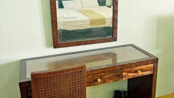 A wooden desk with a glass top, a wicker chair, and a mirror.
