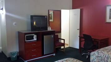 Quarto de hotel com uma cama, uma escrivaninha com cadeira, TV, micro-ondas, frigorífico e lixeira.