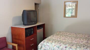 A bedroom with a bed, a wooden dresser with a television on top, a microwave, and a framed picture on the wall.