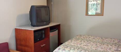 A bedroom with a bed, a wooden dresser with a television on top, a microwave, and a framed picture on the wall.