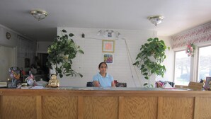 A reception desk with a wooden finish, two potted plants, a framed picture, and a small statue. - Budget Inn Fairport (Fairport)
