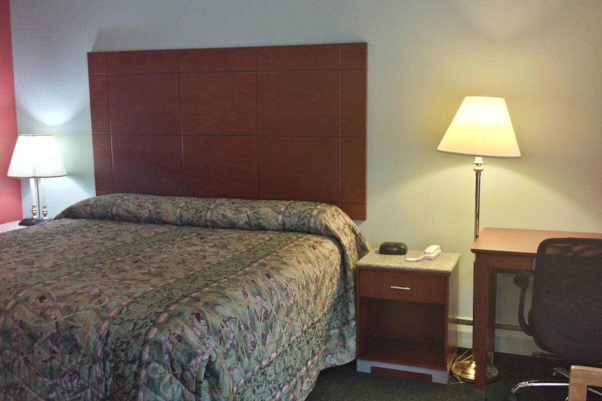 A hotel room with a bed, bedside lamps, a desk with a chair, and a telephone.