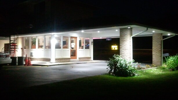 A well-lit building with a covered entrance, a visible door, and a small garden area with plants. - Budget Inn Fairport (Fairport)