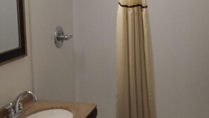 A bathroom with a sink, mirror, shower curtain, and a towel on the floor.
