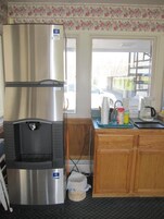 Una cocina con un refrigerador de acero inoxidable, un dispensador de agua, armarios de madera y una ventana con vista a la calle.