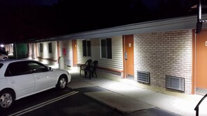 A motel with a white car parked in front, a covered outdoor seating area, and a brick facade.