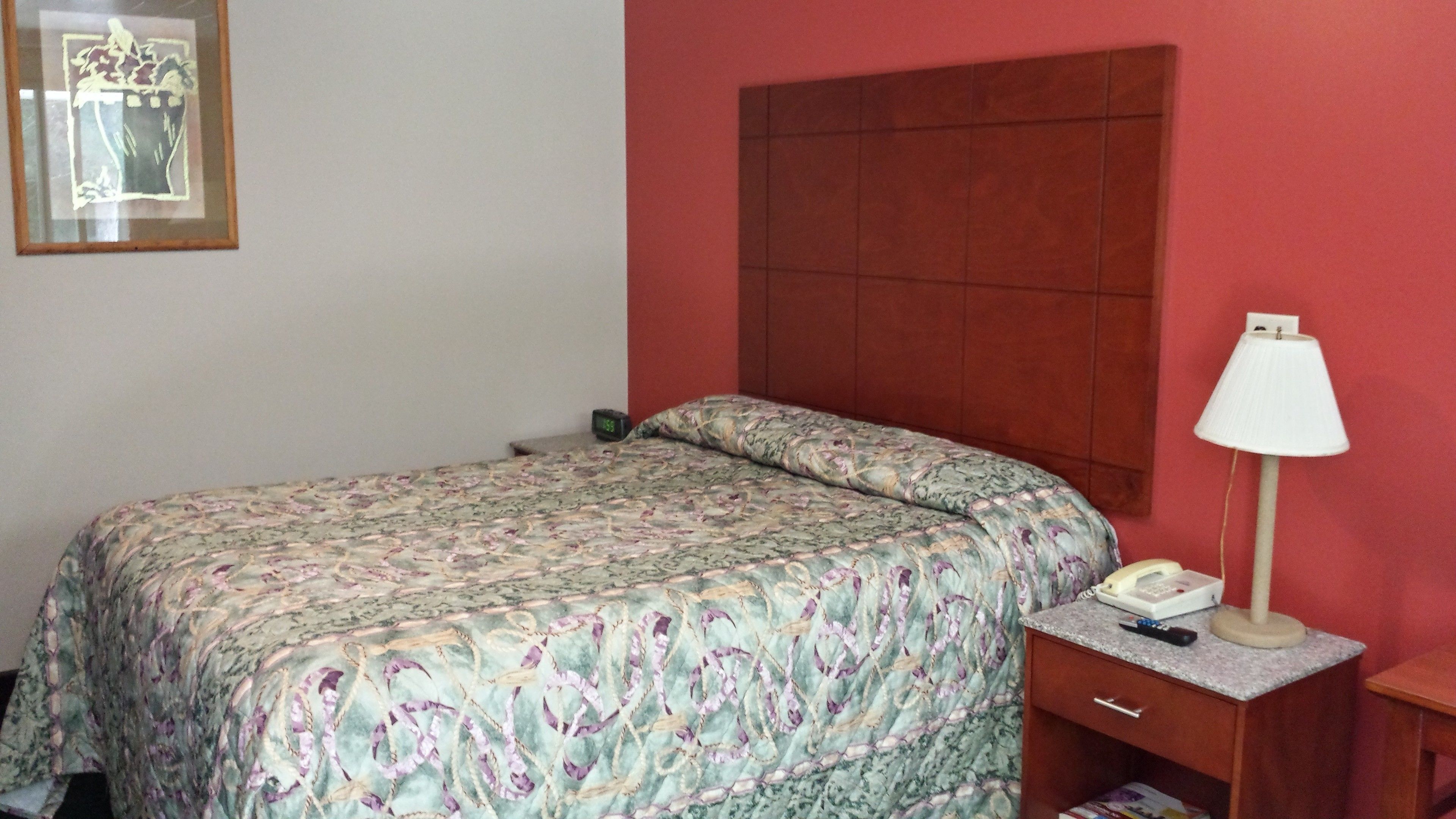Een slaapkamer met een bed, nachtkastje, lamp en een lijst aan de muur.