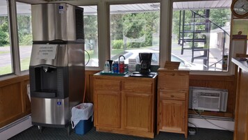 Un área de cocina con un refrigerador de acero inoxidable, una máquina de café y una ventana con vista al estacionamiento y árboles.